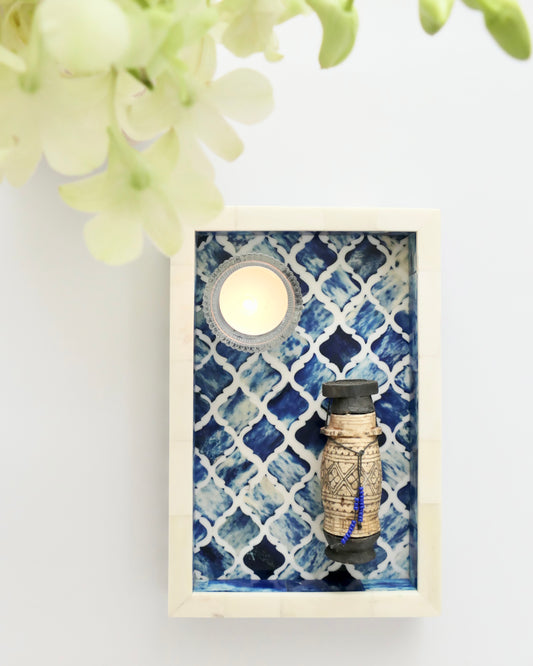 Decorative wall art with a candle and bottle against a blue patterned background
