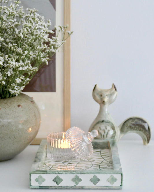 Decorative setting with a candle, vase, and ceramic fox figurine on a white surface.