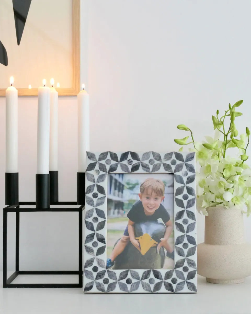Decorative photo frame with a geometric pattern holding a picture of a child, placed on a surface with candles and a plant in the background.