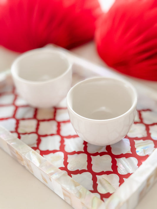 Two white ceramic cups on a red and white checkered cloth with red yarn in the background.