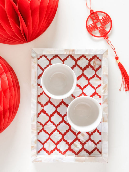 Two white bowls on a red and white patterned tray with red decorative elements in the background.