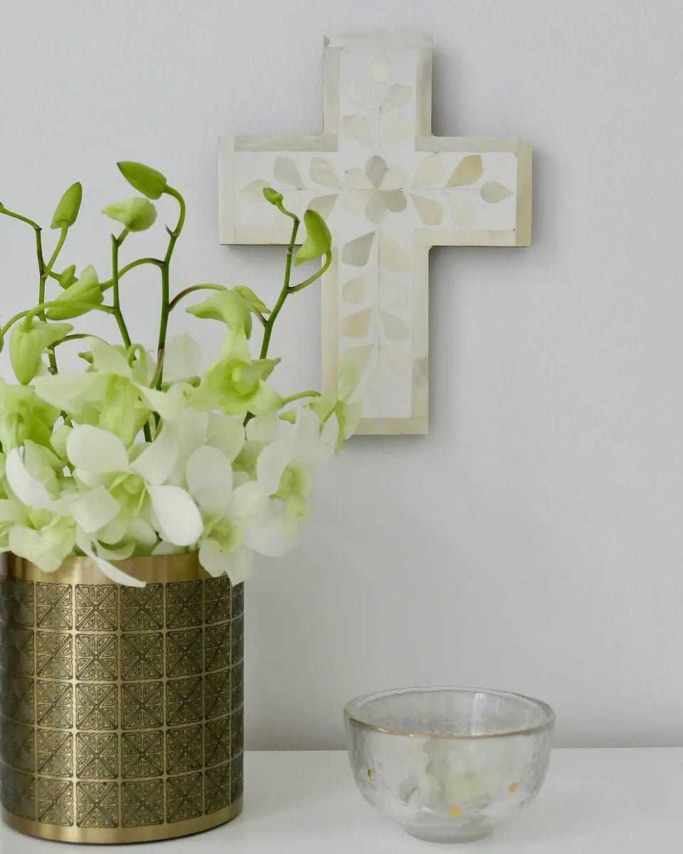 Decorative cross on a wall with a vase of flowers and a small bowl below.