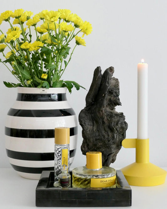 Decorative setup with a striped vase, yellow flowers, a candle, and small bottles on a white background