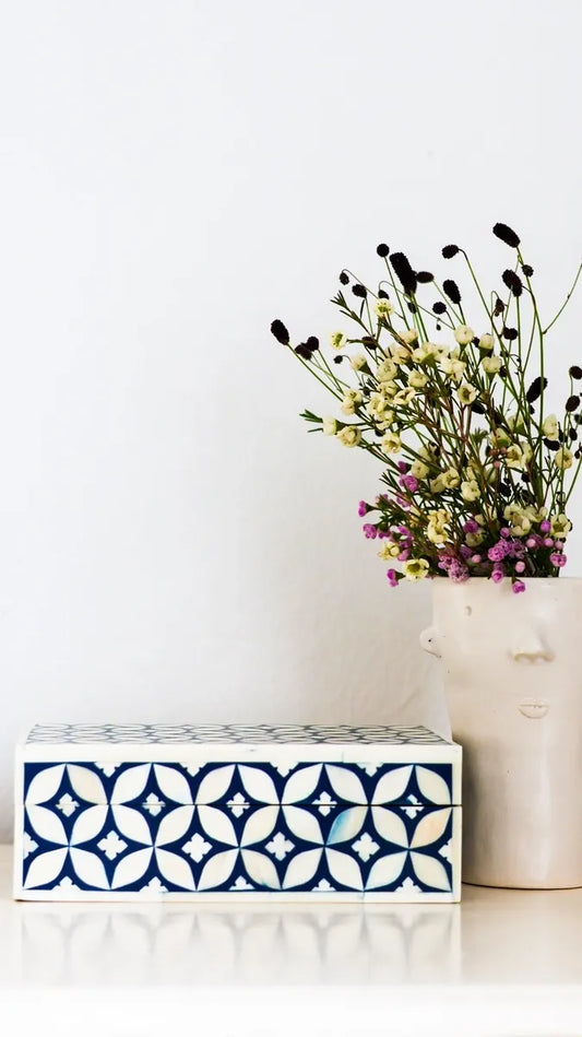 Decorative box with geometric pattern next to a vase with flowers on a white background