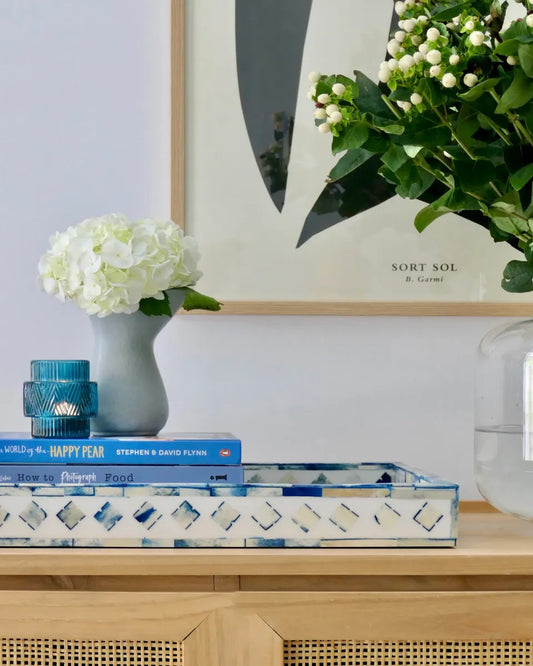 Decorative setting with books, a vase of flowers, and a tray on a wooden surface.