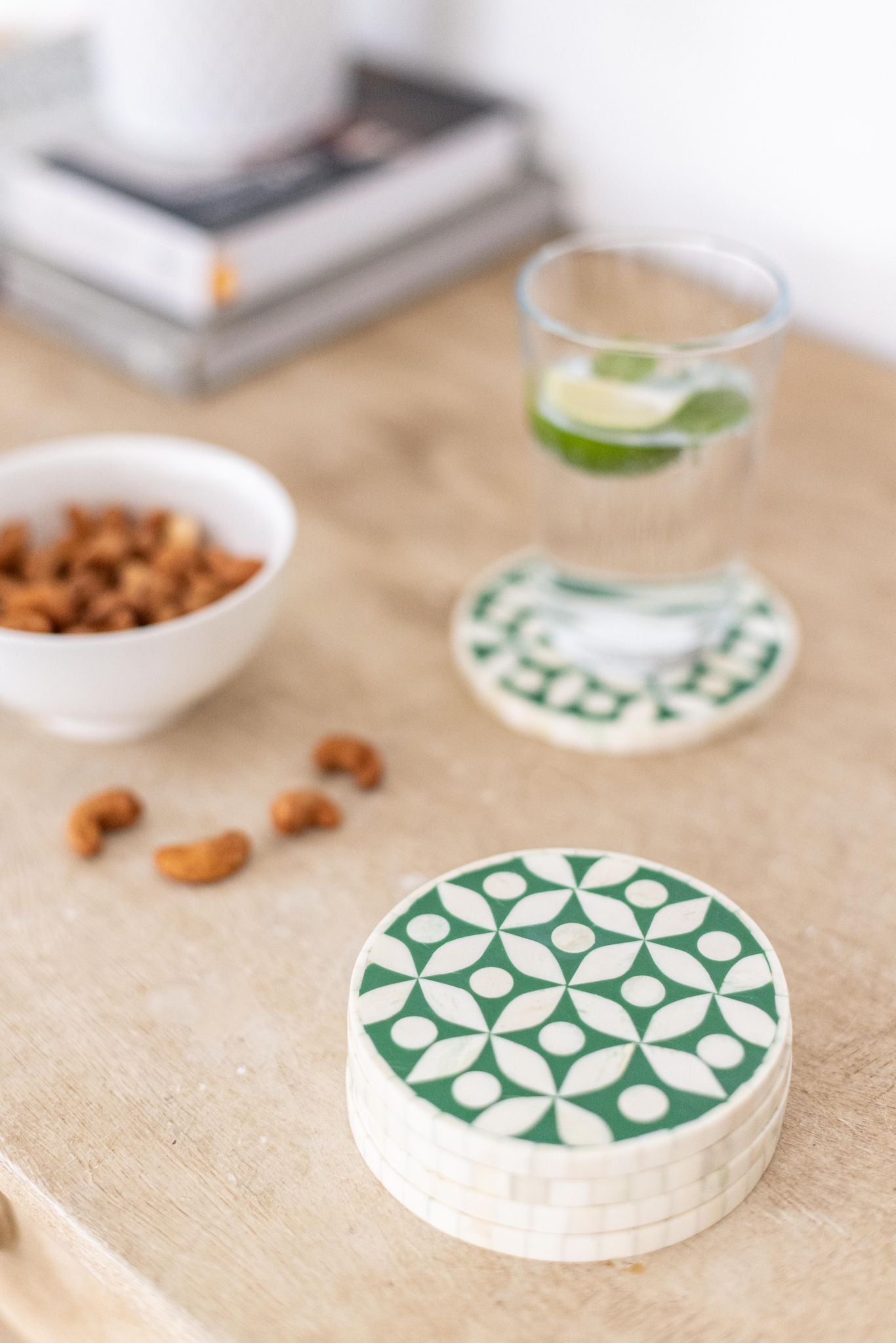 Stack of green and white patterned coasters on a wooden surface with snacks and a glass.