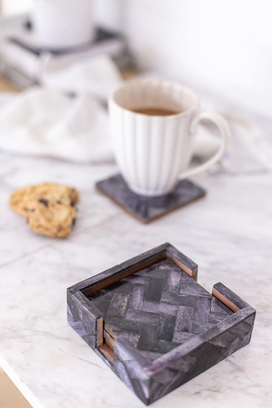 Set of stone coasters with a chevron pattern on a marble surface with a cup of coffee and cookies.