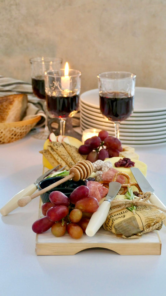 Cheeseboard with grapes, bread, and wine glasses on a table.