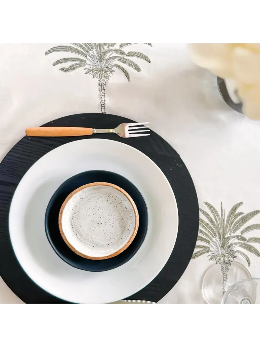 Dining table setting with black and white plates, a small bowl, and a fork on a decorative tablecloth.