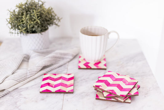 Set of pink and white chevron patterned coasters with a mug on a marble surface.