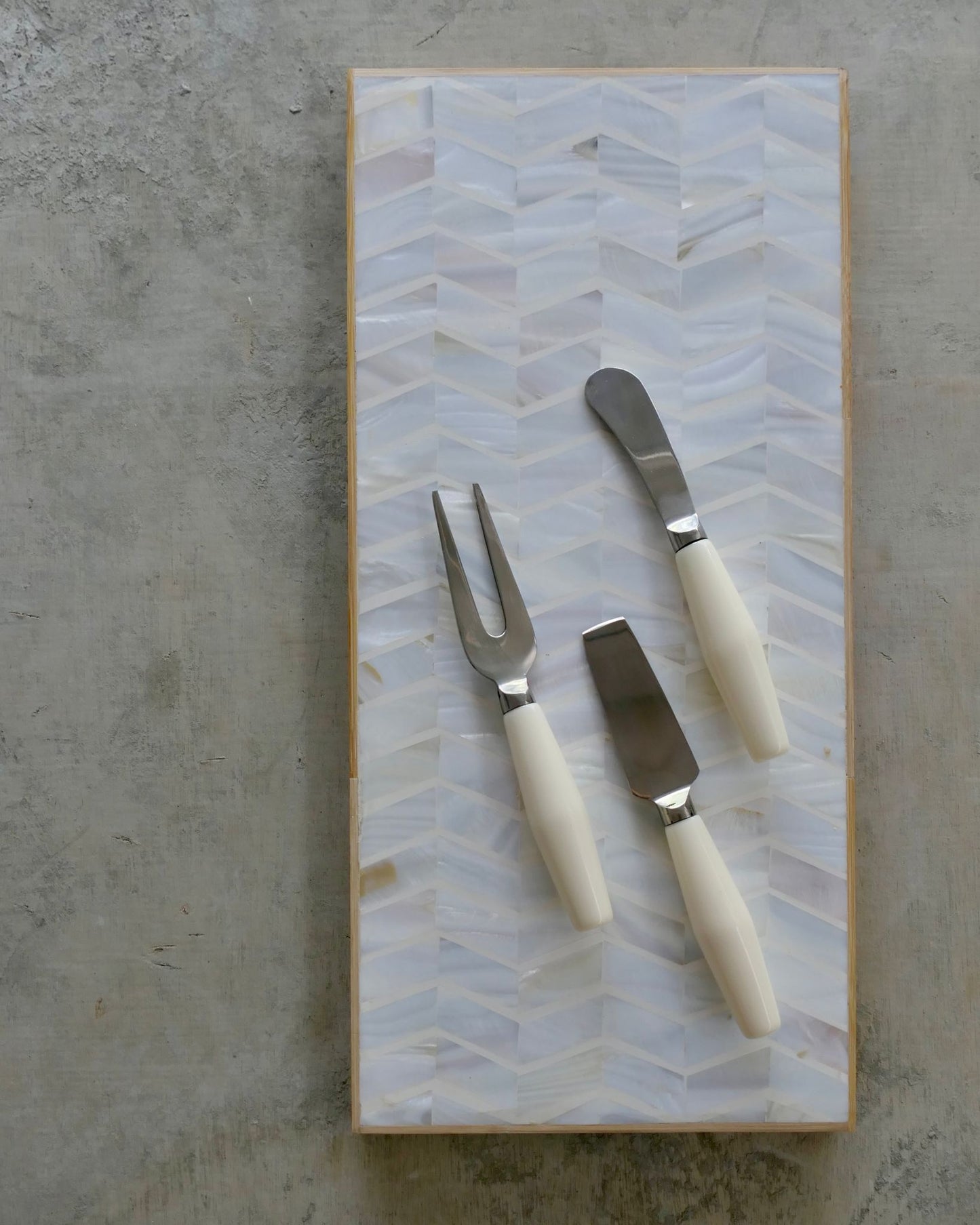 Set of three utensils with white handles on a decorative cutting board with a geometric pattern.