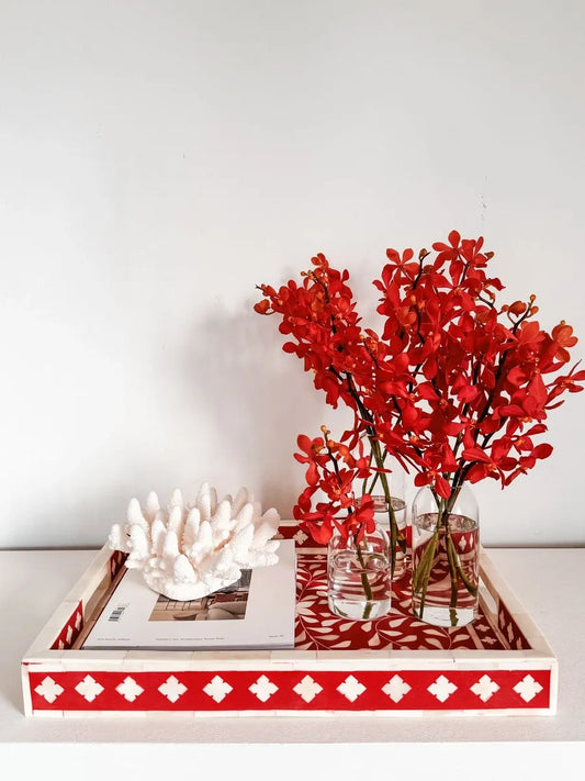 Decorative tray with red flowers, a white ceramic piece, and a red and white patterned cloth on a light background.