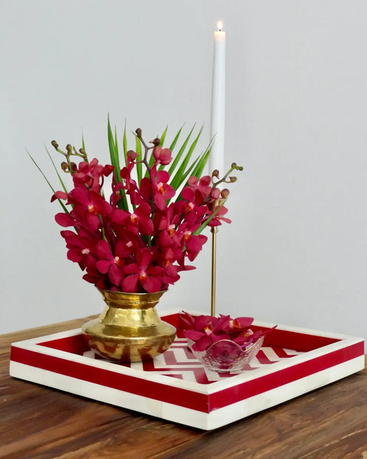 Decorative setup with red flowers in a gold pot on a red and white tray, against a plain background.