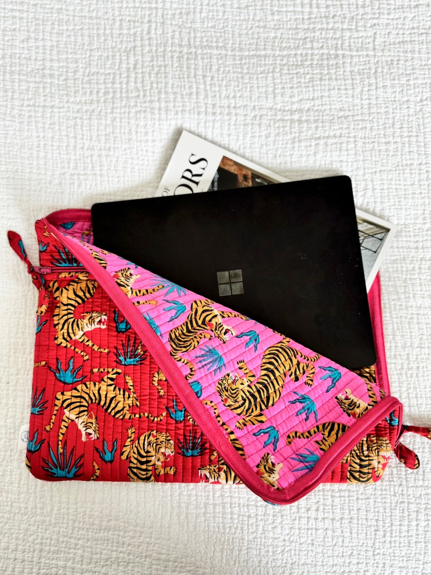 Pink pouch with tiger pattern containing a black laptop on a light gray background