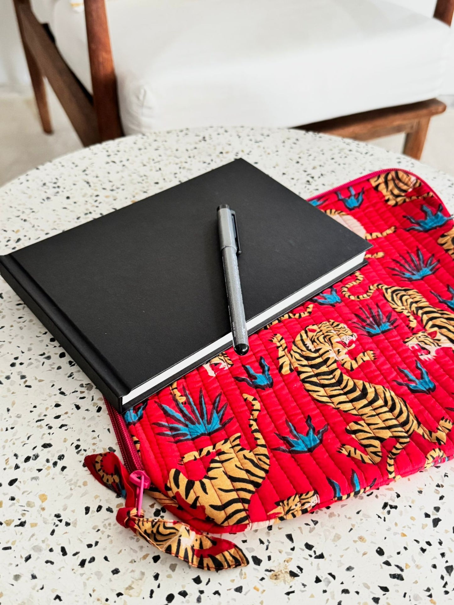 Black notebook with a pen on a red fabric with tiger patterns, placed on a white surface.