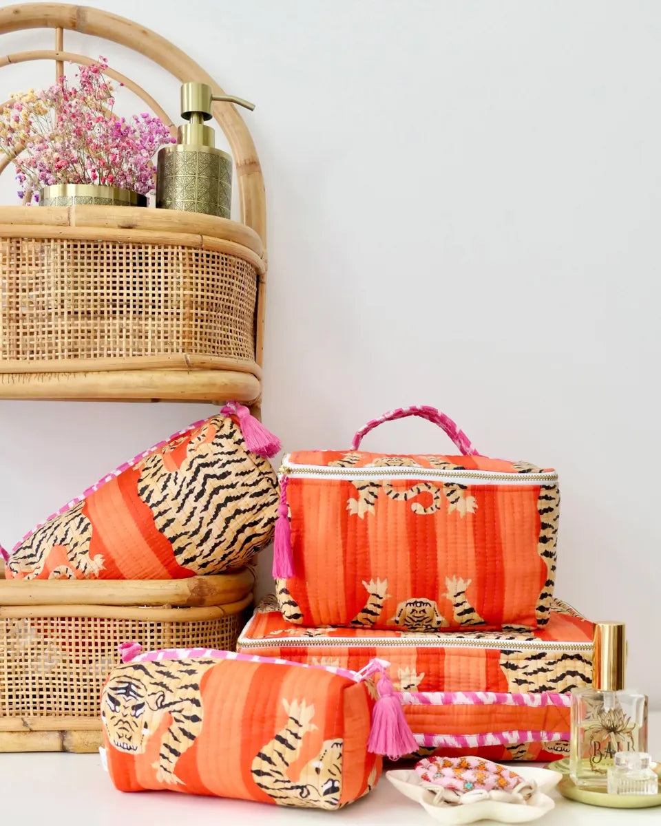 Set of orange and pink striped bags with tiger print on a white surface, with a wicker basket and decorative items in the background.