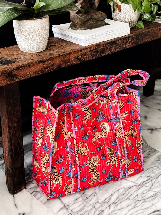 Red tote bag with tiger print on a marble surface next to a wooden bench with plants.