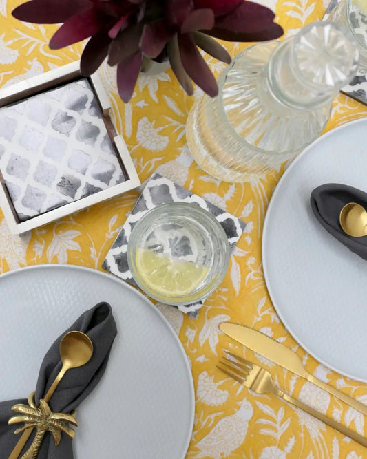 Table setting with yellow tablecloth, white plates, gold cutlery, and decorative elements.