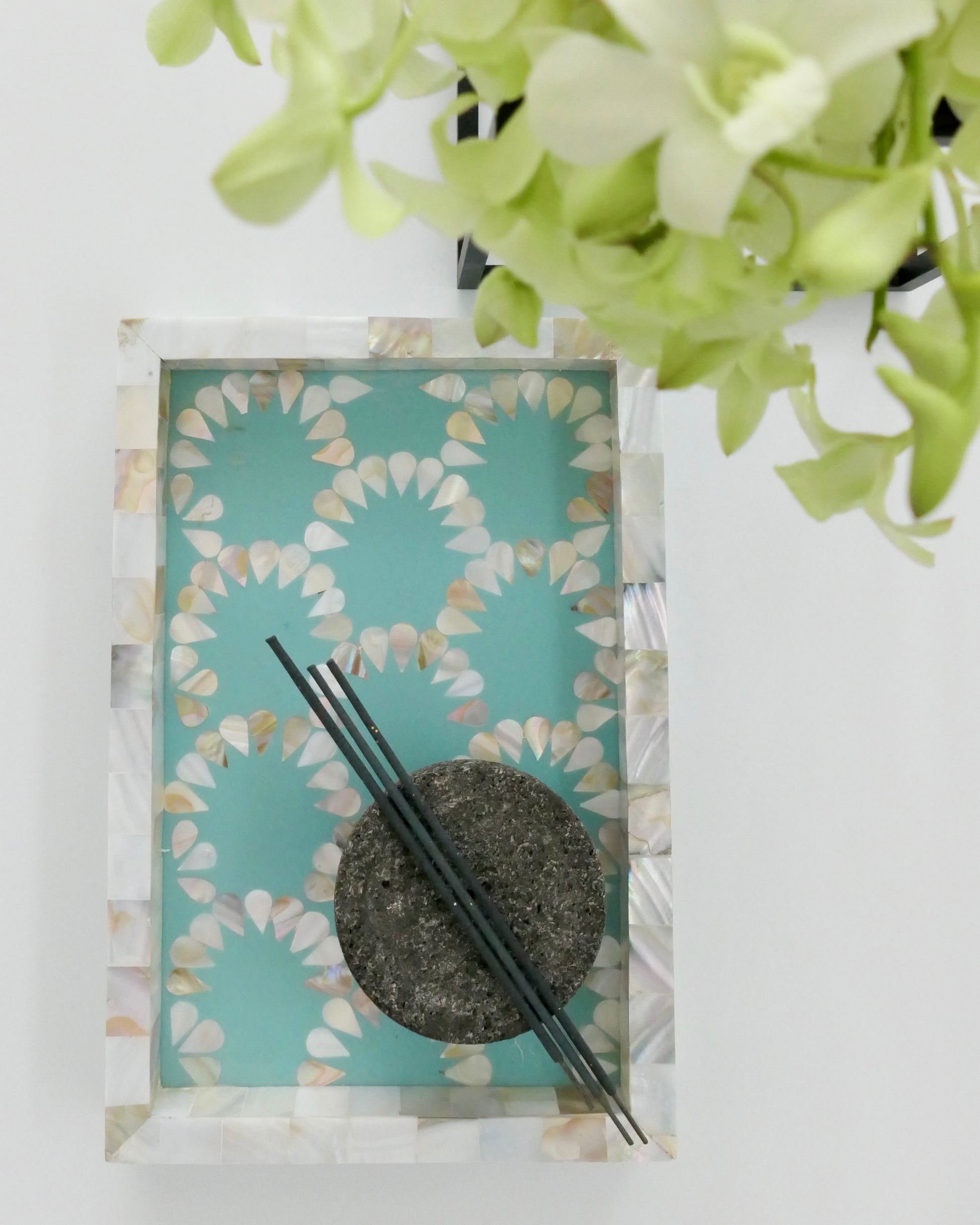 Decorative item with a circular stone, two black sticks, and a floral pattern on a teal background.