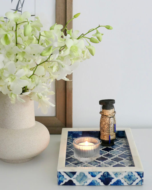 Decorative candle holder with a lantern on a blue and white patterned tray, next to a vase of white flowers.