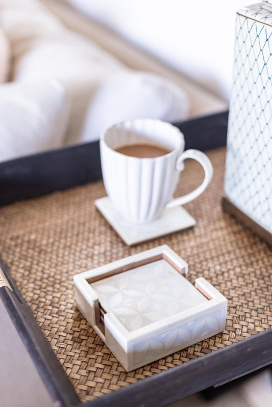White mug with coffee on a woven tray next to a box of coasters.