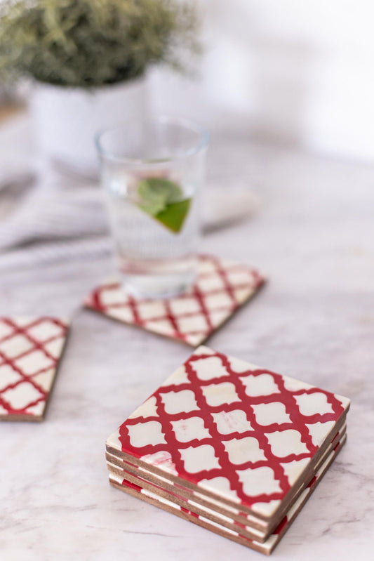 Set of red and white patterned coasters on a light surface with a glass of water and plant in the background.