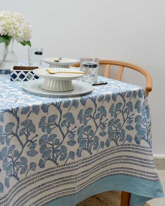 Table with a blue and white floral-patterned tablecloth, featuring a cake stand and glasses.