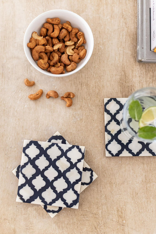 Bowl of cashews on a textured surface with coasters and a glass of water.