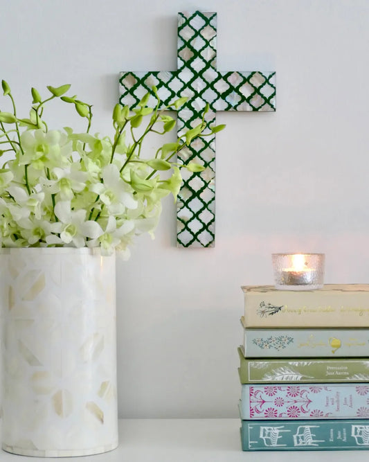 Decorative cross on a wall with a vase of flowers and books below.