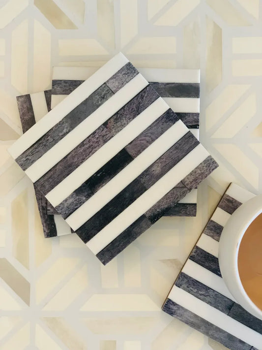 Grey and white striped coasters on a geometric-patterned surface with a cup of coffee.