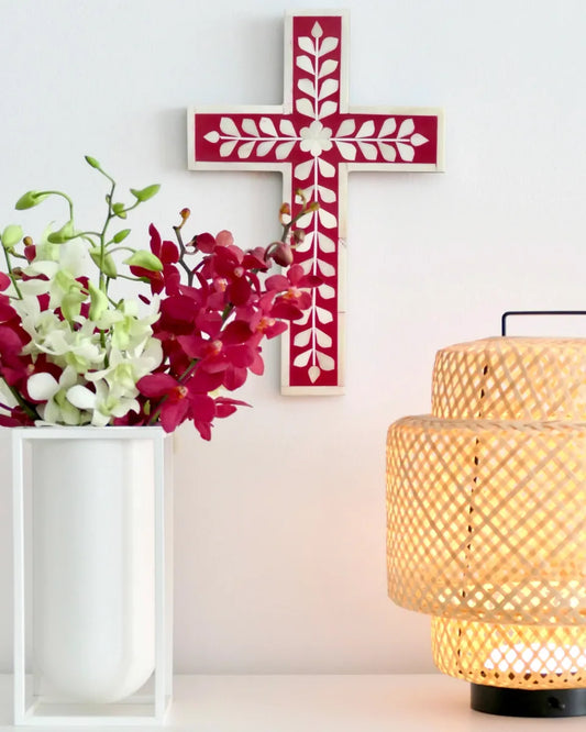 Decorative cross with floral arrangement and lamp on a white wall