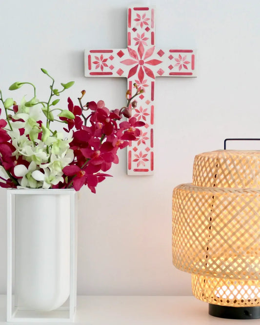Decorative cross with floral patterns, a vase of flowers, and a woven lantern on a light background