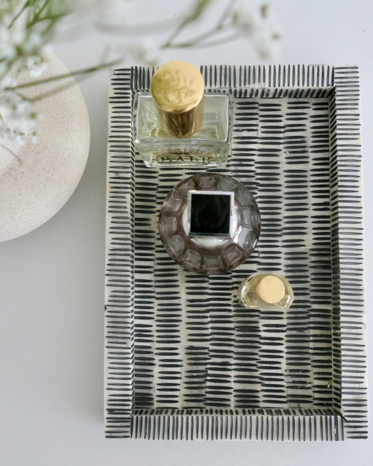 Decorative tray with a glass container, gold bottle cap, and small round object on a white surface.