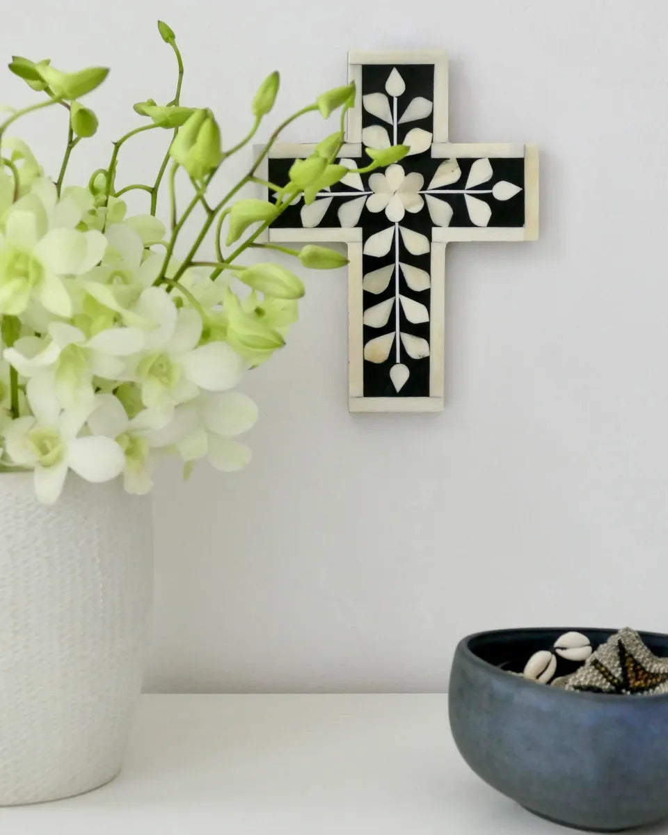 Decorative cross with floral patterns on a white wall, next to a vase with flowers and a bowl.