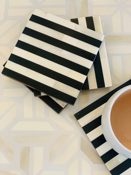 Black and white striped coasters on a geometric-patterned surface with a cup of coffee.