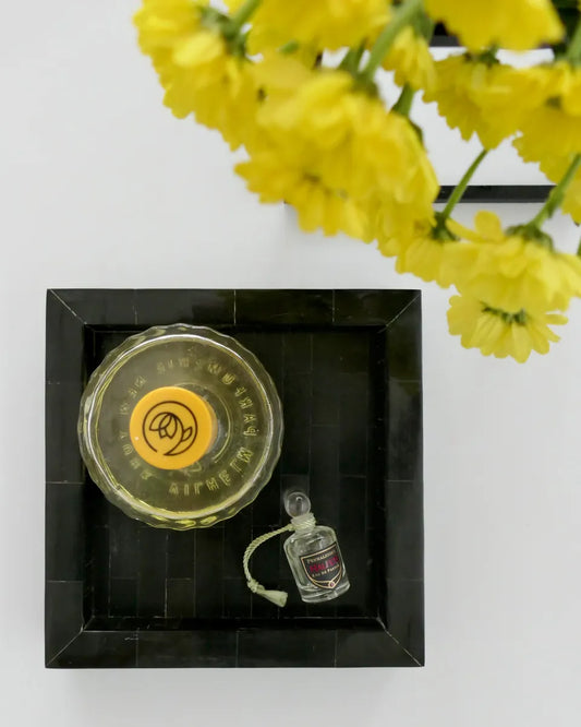 Small round container with yellow lid and a miniature bottle inside, framed by yellow flowers on a white background.