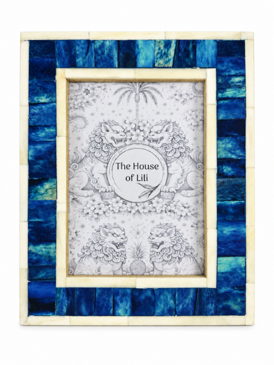 A rectangular picture frame with a blue and teal striped mosaic outer border and a light beige inner frame, holding a decorative black-and-white illustration with the text 'The House of Lili' in the center.