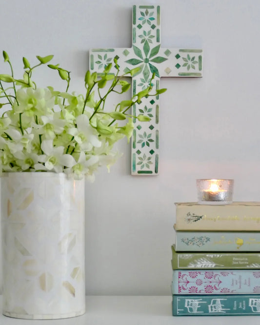 Decorative cross with floral patterns, a vase with flowers, and books on a white surface.