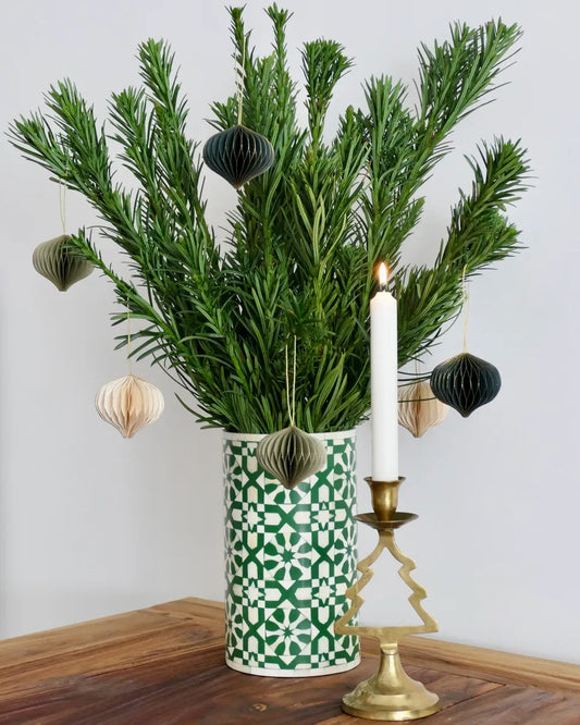 Decorative arrangement with greenery, a candle, and ornaments in a patterned vase on a wooden surface.