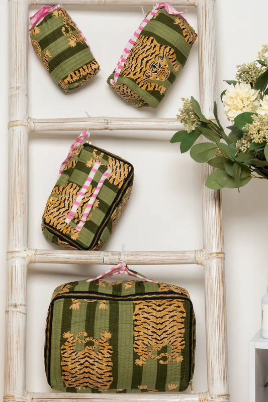 Set of green and gold patterned pouches on a white surface with flowers in the background