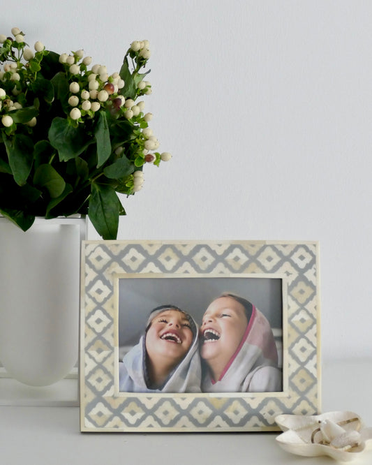 Decorative picture frame with a photo of two people laughing, next to a vase of white flowers on a light background.