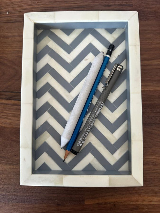 Three pens on a chevron-patterned tray with a wooden frame.