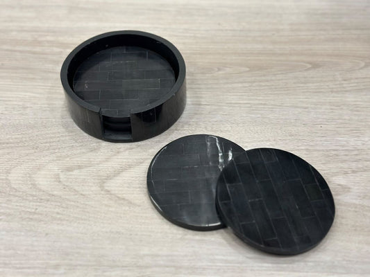 Three black circular coasters with textured surface on a wooden surface