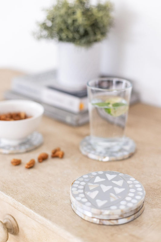 Decorative coasters on a wooden surface with a glass of water and a bowl in the background.