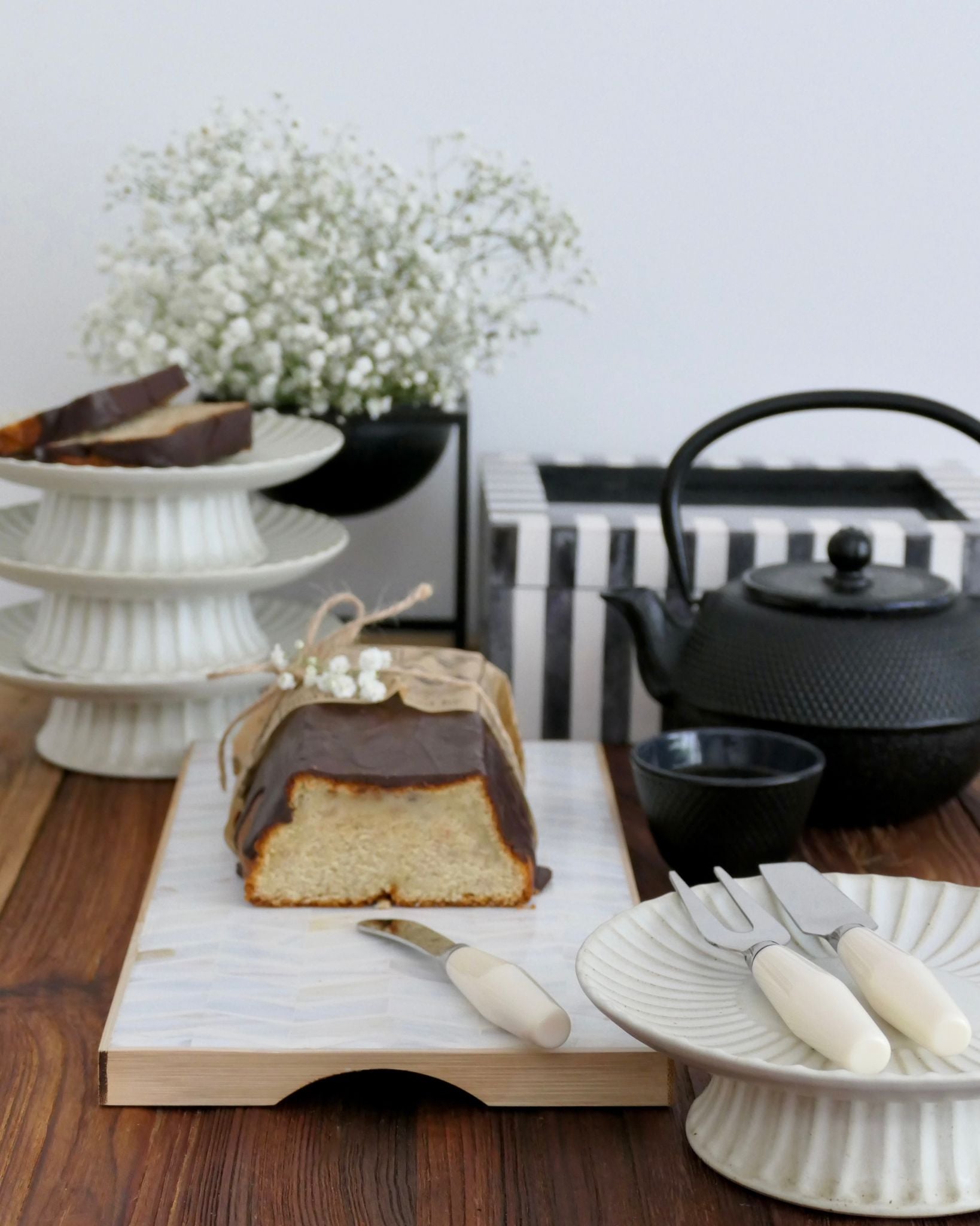 Sliced cake on a wooden board with a teapot and flowers in the background