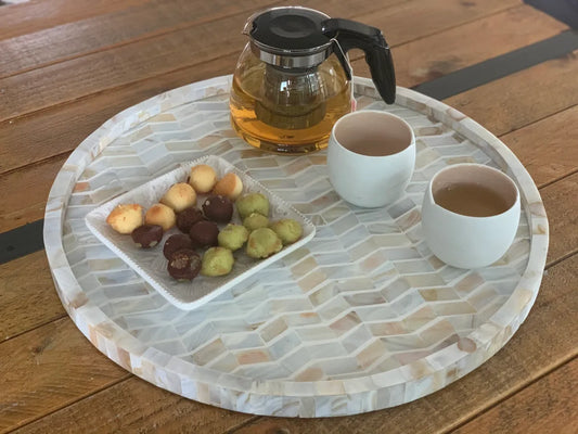 Round stone tray with fruit, cups of tea, and a teapot on a wooden surface
