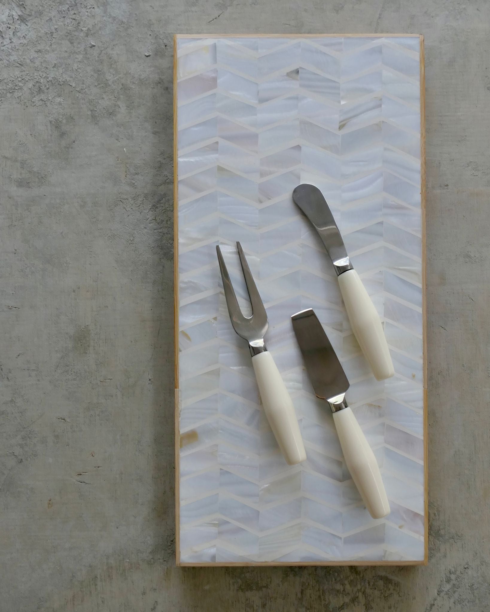 Set of three utensils with white handles on a decorative cutting board with a geometric pattern.
