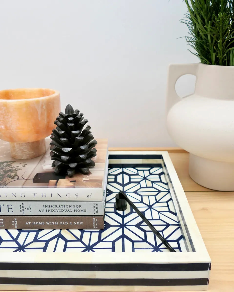 Decorative tray with books, a pine cone, and a candle on a wooden surface.