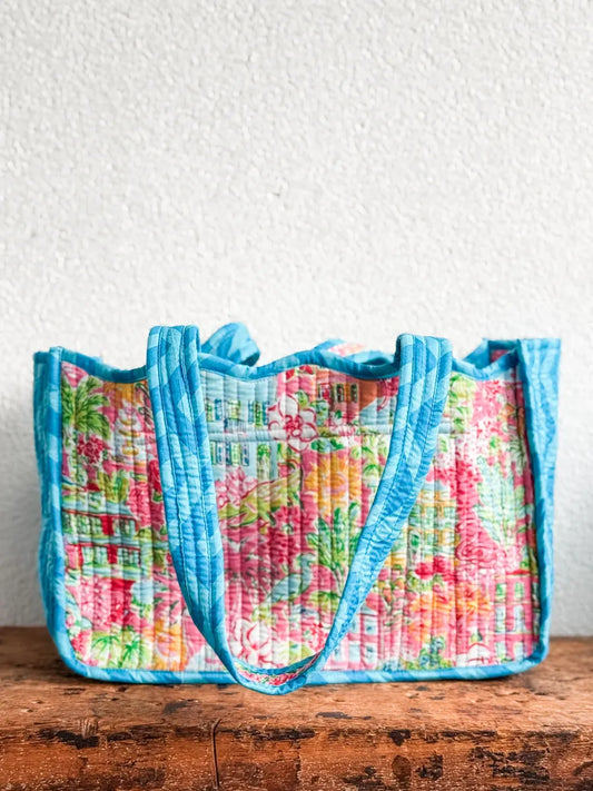 Floral-patterned quilted bag with blue trim on a wooden surface