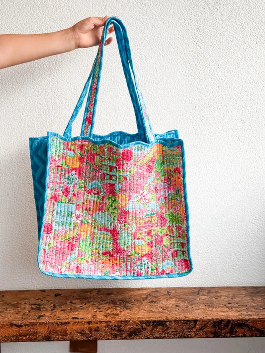 Colorful floral-patterned tote bag with blue handle held by a hand on a wooden surface.